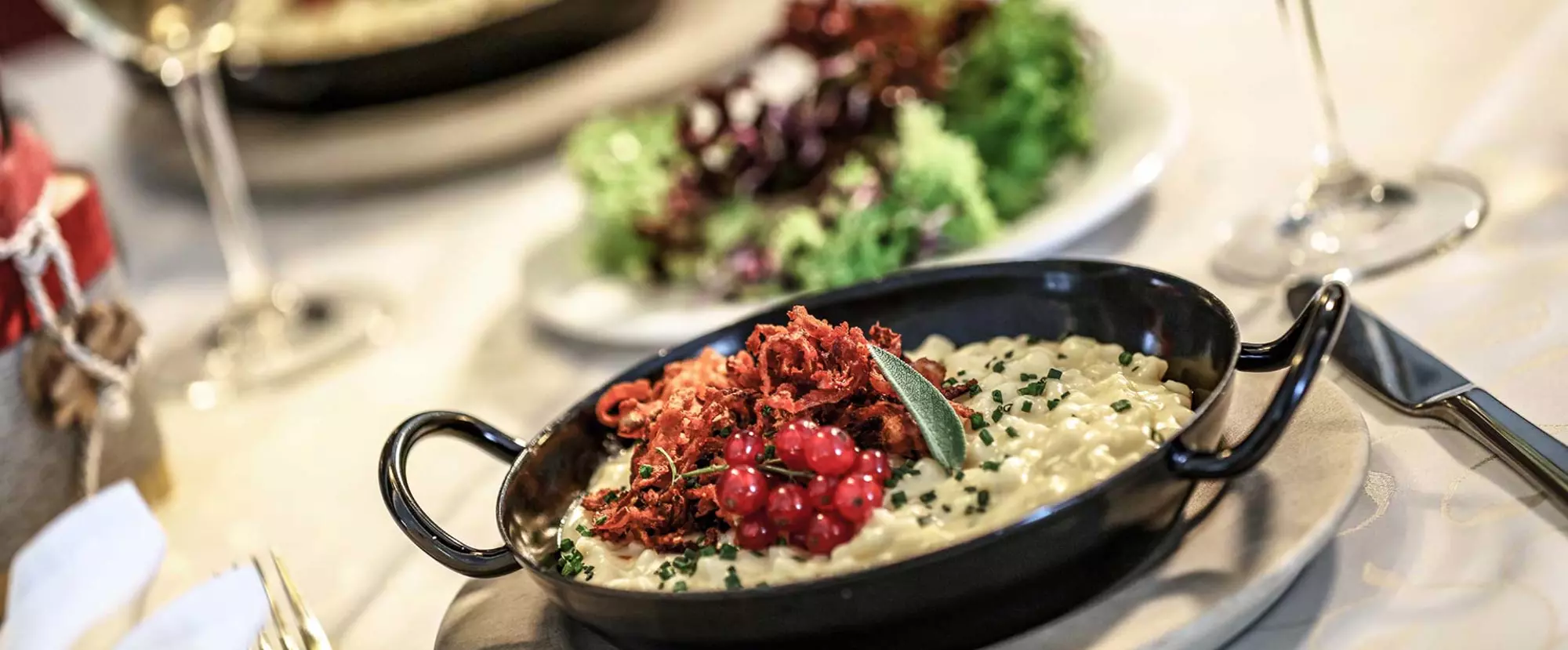 Käsespätzle mit Röstzwiebeln und Johannisbeeren in einer schwarzen Pfanne mit kleinem Salat