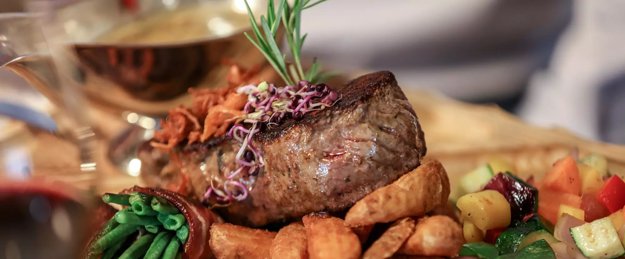 Gebratenes Steak mit Sprissen und Rosmarin auf Speckbohnen, Kartoffelwedges und Grillgemüse